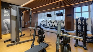 Un gimnasio con equipamiento de levantamiento de pesas, cintas de correr y un cartel motivacional.