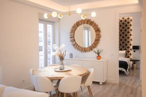 A dining area with a round wooden table, white chairs, a vase with flowers, and a large mirror on the wall. - Escape to Urban Charm: Apartment with Balcony and Modern Spaces (Madrid)