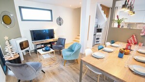 A modern living room with a TV, seating, and a dining area with a table set for two. - Beautiful villa in Lomener-beach, restaurants, and shops within walking distance (Ploemeur)