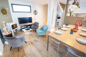 A modern living room with a TV, seating, and a dining area with a table set for two.