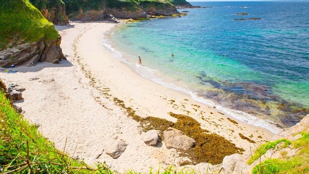 Una playa con agua turquesa cristalina, orilla arenosa y afloramientos rocosos.