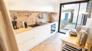 A modern kitchen with white cabinets, a wooden countertop, and a large window offering a view of the outside. - Beautiful villa in Lomener-beach, restaurants, and shops within walking distance (Ploemeur)