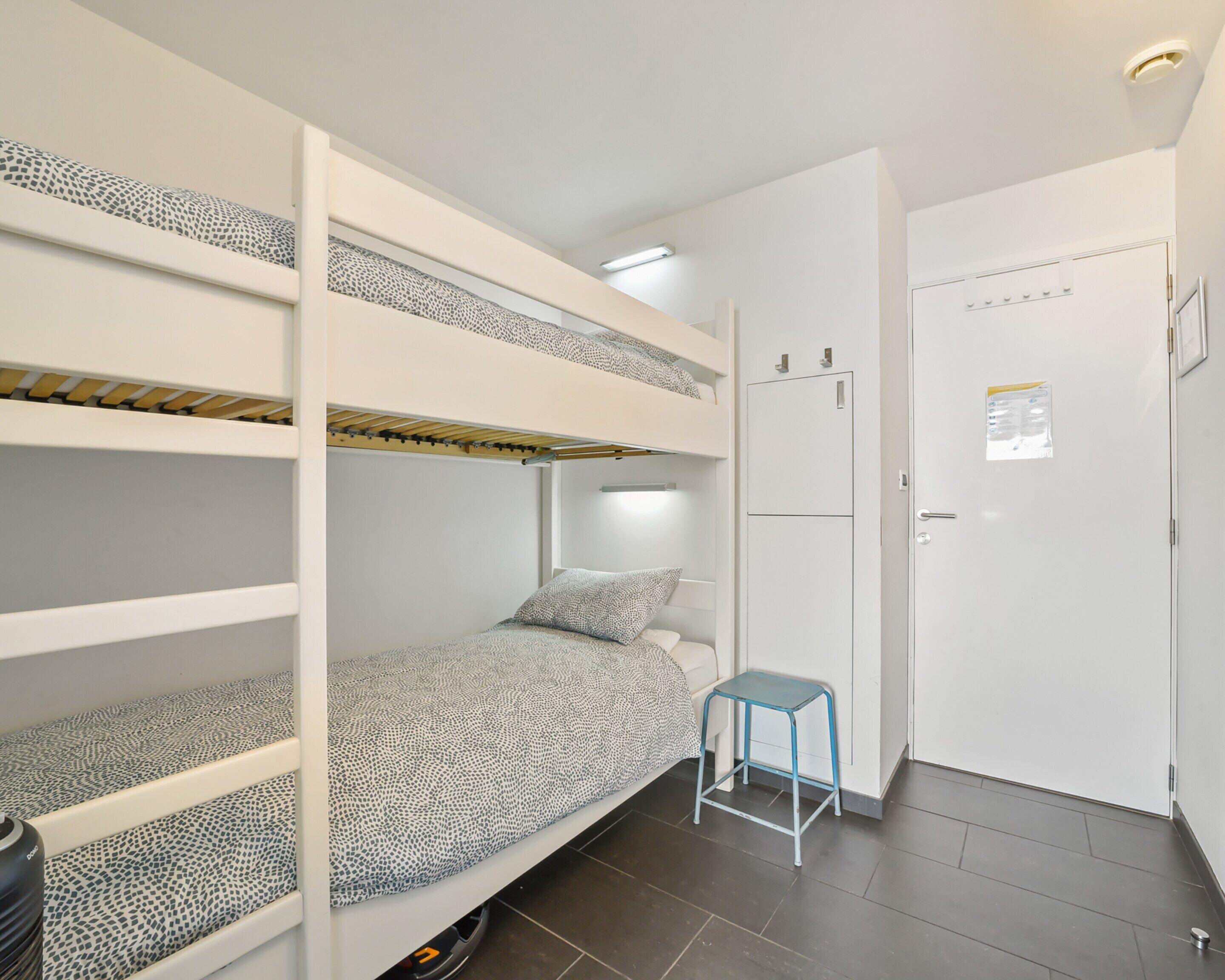 A bunk bed room with a small stool, a door with a light switch, and a tiled floor.