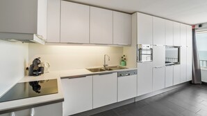 A modern kitchen with white cabinets, a stainless steel sink, and a built-in oven. - Spacious Studio With sea View (Blankenberge)