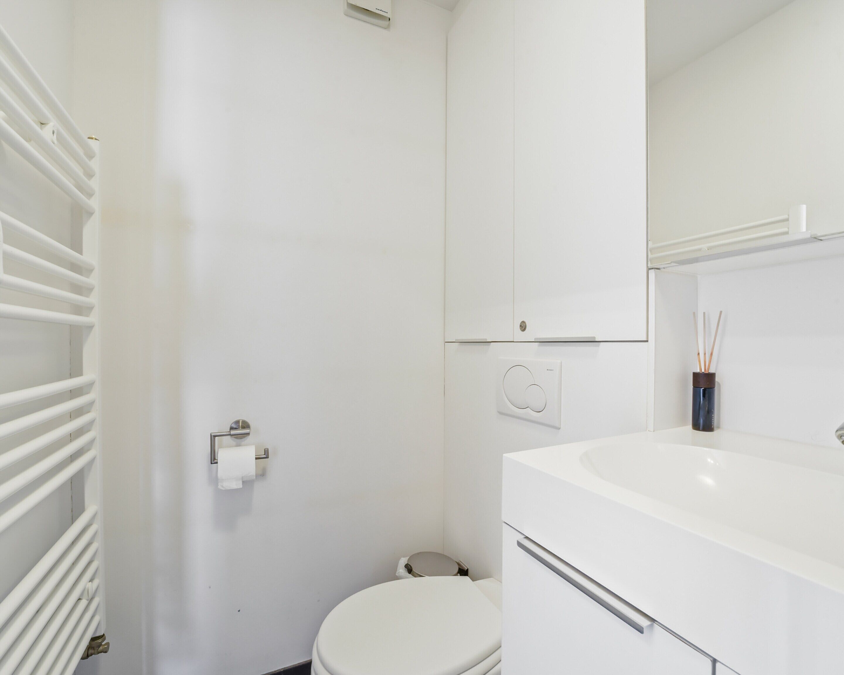 Une salle de bain moderne avec des toilettes, un lavabo blanc et un porte-serviettes.