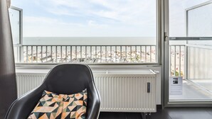 A room with a view of a beach, a black chair with a patterned cushion, and a white radiator. - Spacious Studio With sea View (Blankenberge)