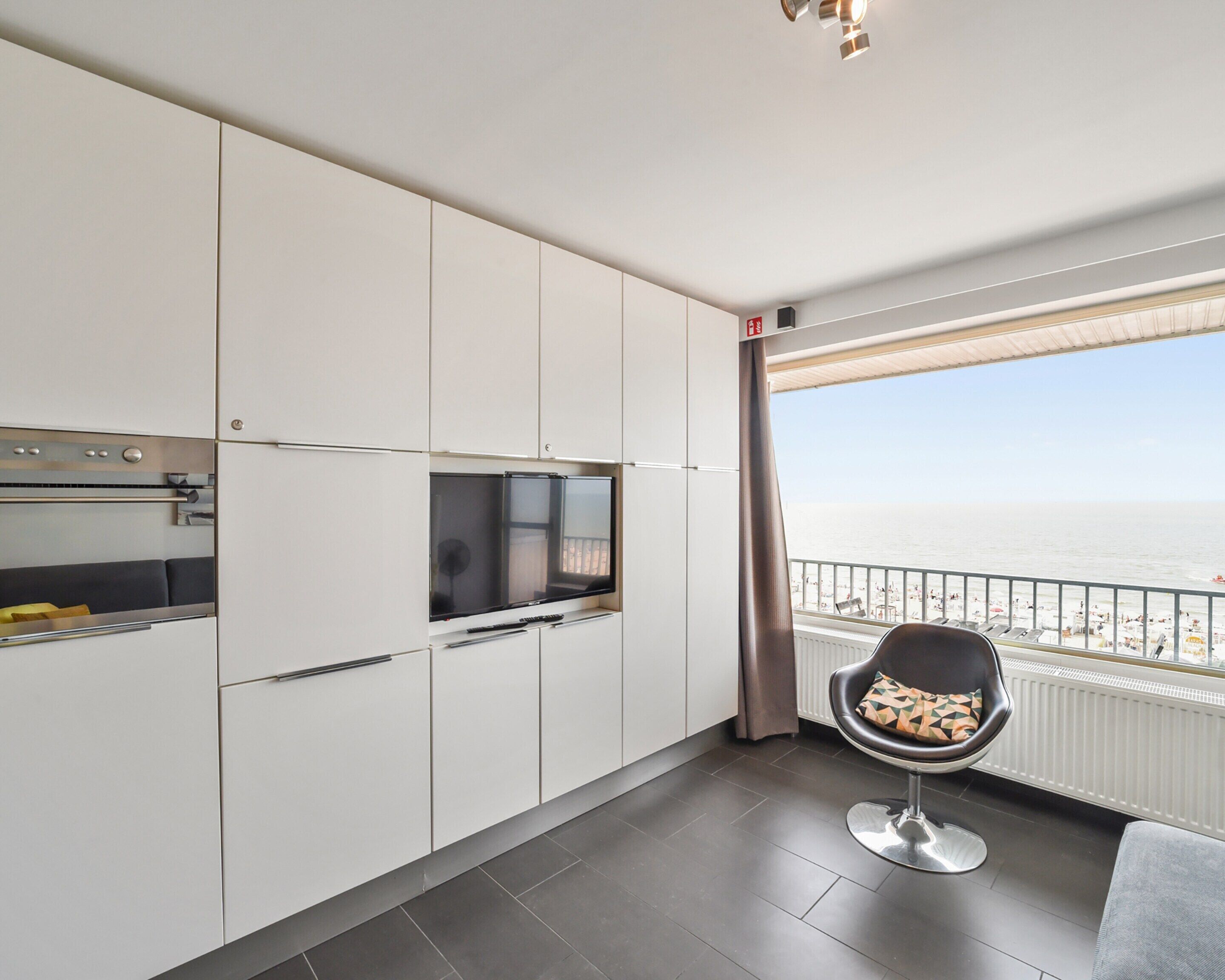 A modern kitchen with white cabinetry and a large window overlooking the beach.