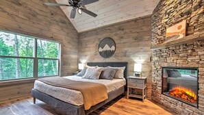 Un dormitorio con cama, chimenea de piedra, mesita de noche y ventana con vista a árboles.