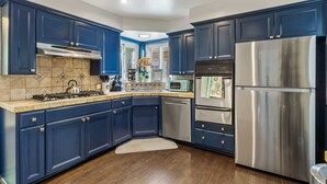 A modern kitchen with dark blue cabinets, stainless steel appliances, and a tiled backsplash. - Charming Downtown Bungalow | Easy Airport Access (San Diego)