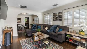 A spacious living room with a dark grey sofa, a coffee table, and a bookshelf. - Charming Downtown Bungalow | Easy Airport Access (San Diego)
