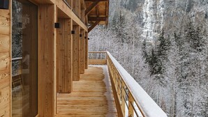 Un balcón de madera con vista a un bosque nevado y una cascada.