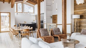Un amplio salón con techo alto, vigas de madera, una mesa de comedor con sillas, un sofá y una chimenea.