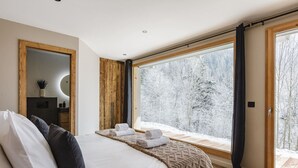 Un dormitorio con un ventanal grande, una cama con almohadas, una mesita de noche y un espejo.