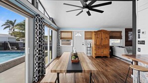 Una cocina moderna con una mesa y banco de madera, un ventilador de techo y vista a una piscina.