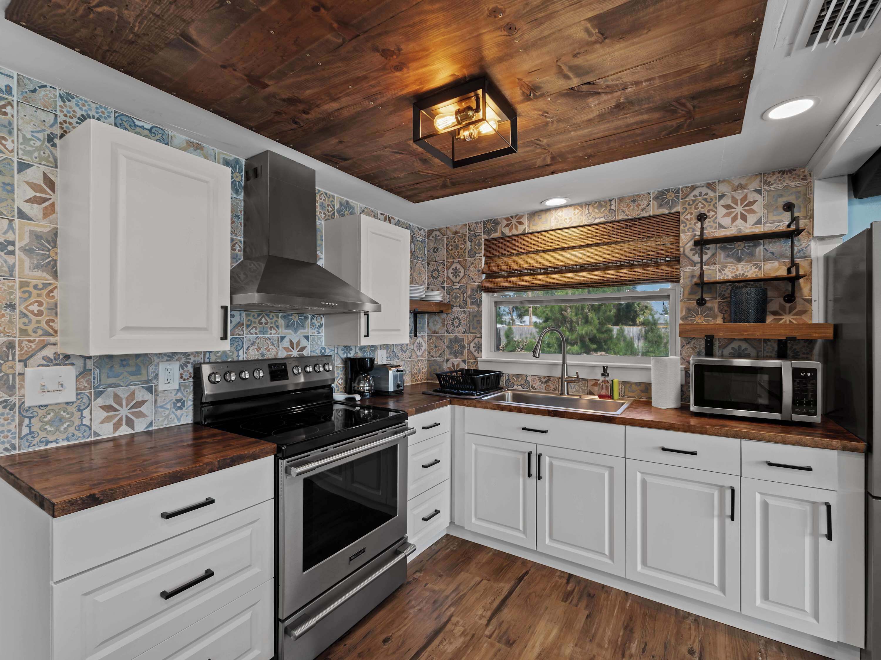 A modern kitchen with white cabinets, a stainless steel stove, and a wooden ceiling.