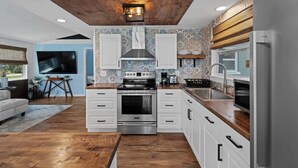 Una cocina moderna con armarios blancos, estufa de acero inoxidable y techo de madera.