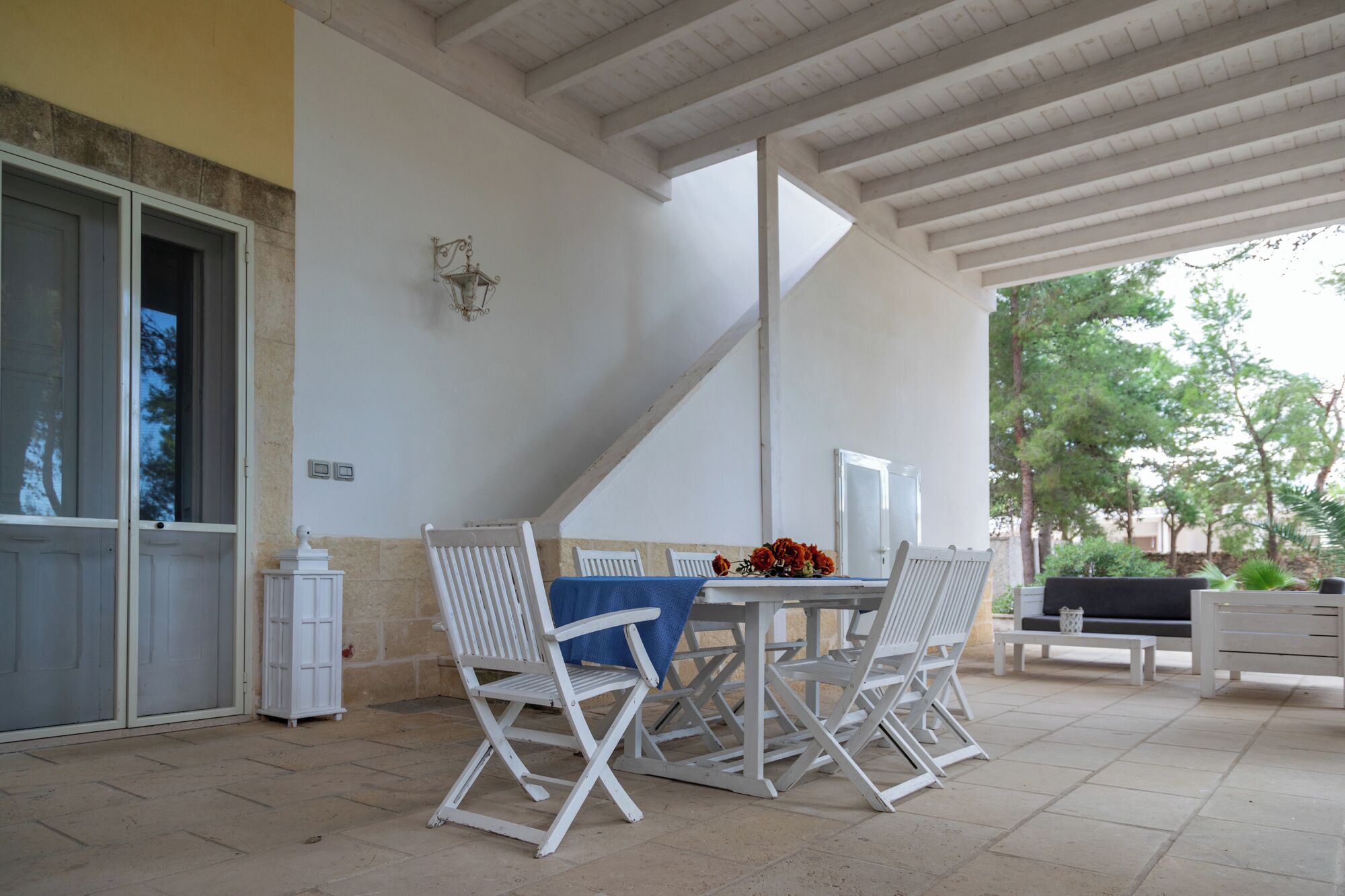 A covered patio with a table and chairs, a bench, and a wall-mounted light fixture.