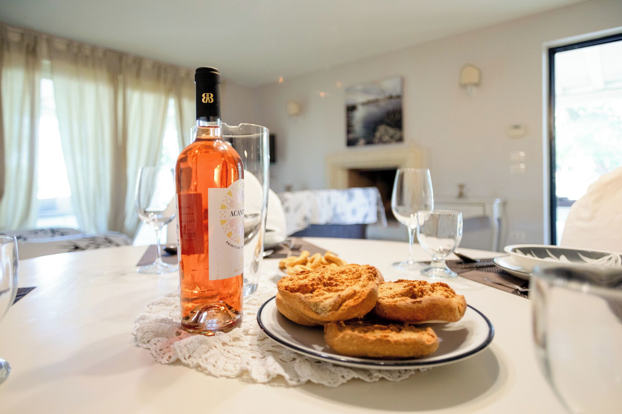 A dining table with a bottle of wine, a plate of pastries, and glasses.