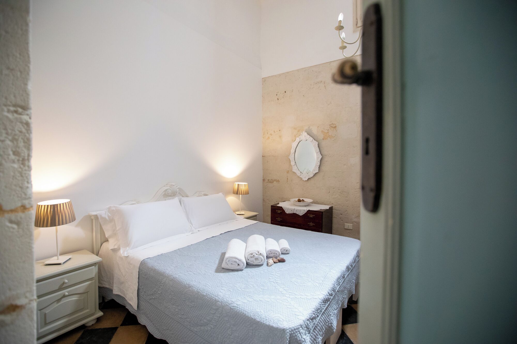 A hotel room with a bed, bedside tables, a mirror, and a door.