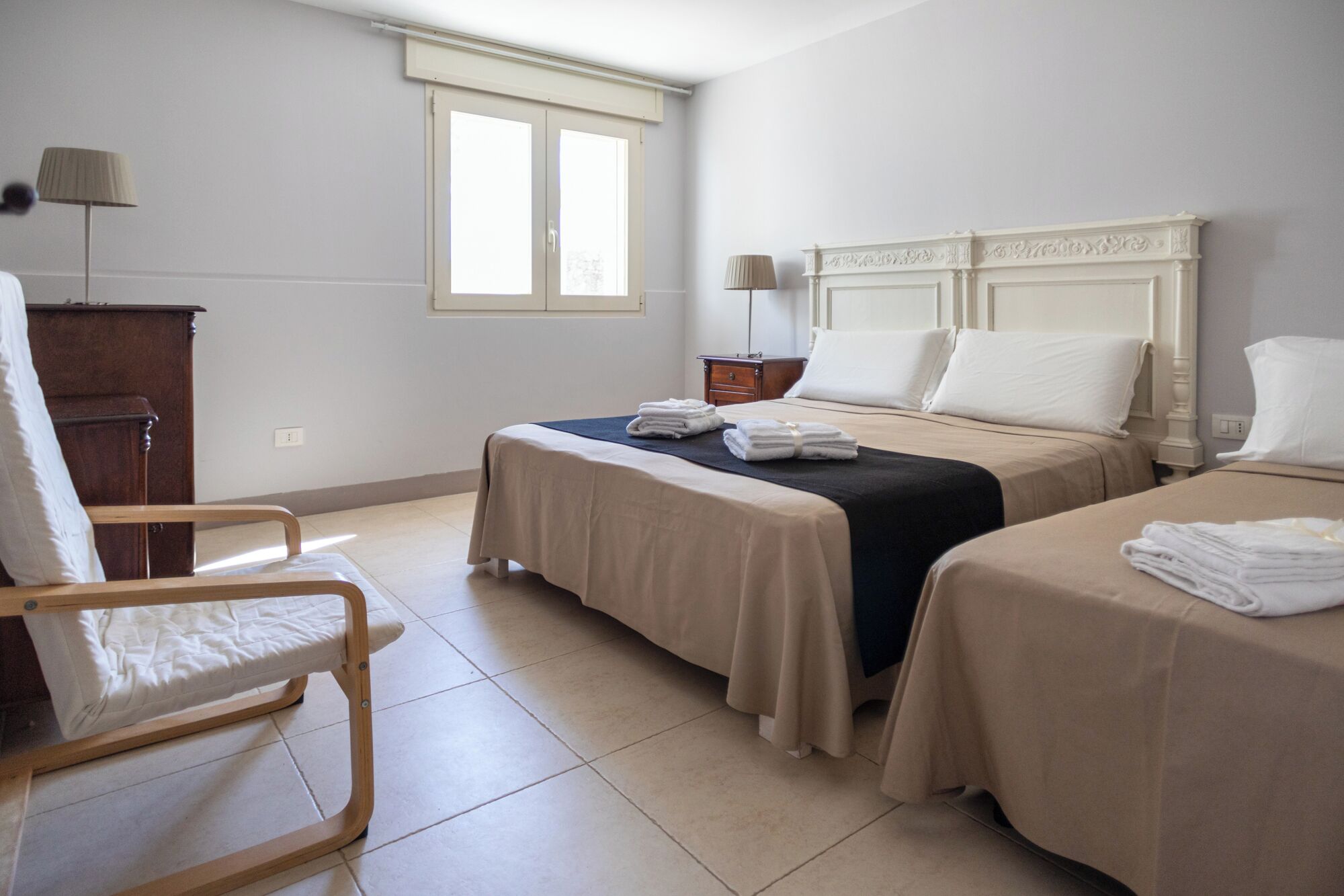 A hotel room with two beds, a wooden chair, a desk, and a window.