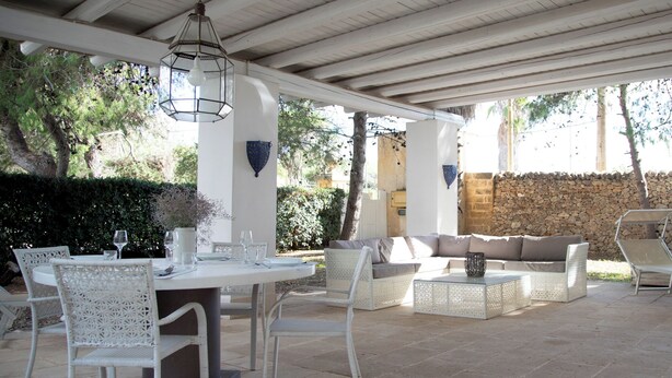 An outdoor patio area with a round table and chairs, a sofa, and a stone wall in the background. - Villa La Tonnara (Porto Cesareo)