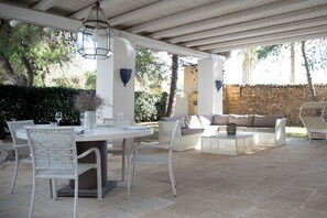 An outdoor patio area with a round table and chairs, a sofa, and a stone wall in the background. - Villa La Tonnara (Porto Cesareo)