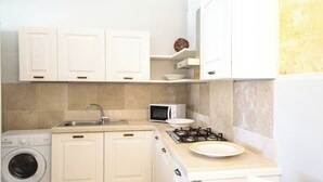 A compact kitchen with white cabinets, a washing machine, a microwave, and a gas stove. - Villa La Tonnara (Porto Cesareo)