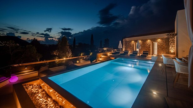 Uma área de piscina moderna ao ar livre, com muro de pedra e assentos, rodeada por um terraço bem iluminado.