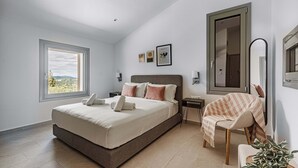 Quarto com cama grande, cadeira, mesa de cabeceira, espelho e janela com vista para o exterior.
