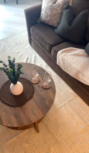 A round wooden coffee table with a white vase and two wine glasses on a brown placemat. - French Inspired Stay Fireplace Coffee bar Cozy (Englewood)