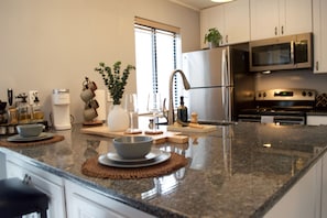 A modern kitchen with granite countertops, stainless steel appliances, and a large window providing natural light. - French Inspired Stay Fireplace Coffee bar Cozy (Englewood)