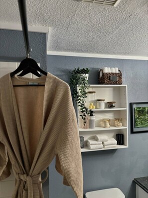 Ein Badezimmer mit Handtuchhalter, Ablagefach für Toilettenartikel, einer Topfpflanze und einem gerahmten Bild an der Wand.