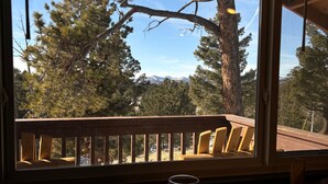 Ein Tisch mit zwei leeren Weingläsern und Blick auf eine Holzterrasse und Bäume durch ein Fenster.