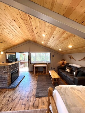 Interior acogedor de una cabaña con chimenea de piedra, techo de madera y un ventanal con vistas a una terraza.