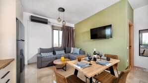 A modern living room with a dining area, a grey sofa, a flat-screen TV, and a wooden dining table with chairs.