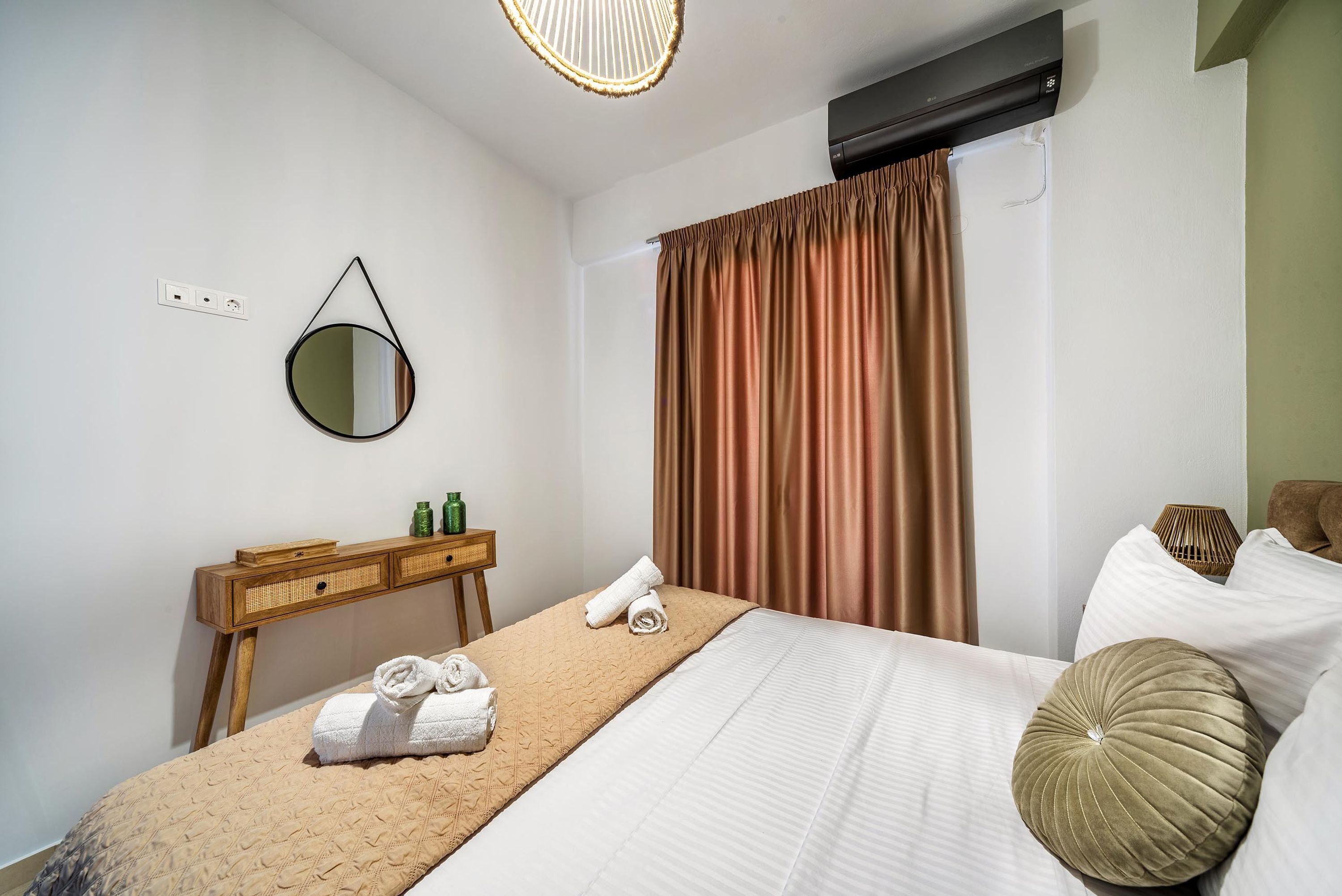 A hotel room with a bed, a bedside table with toiletries, a mirror, and a window with curtains.
