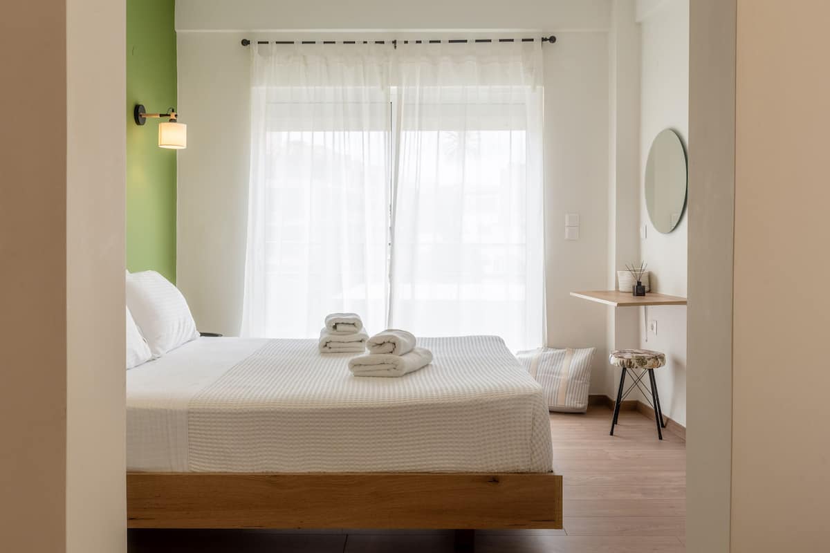 Ein ordentlich gemachtes Bett mit weißen Leinen und gerollten Handtüchern, ein Nachttisch mit Lampe und ein kleiner Hocker.
