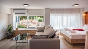 A modern room with a sofa, a bed, a glass table, and a potted plant. - Senaon Urban Living City Center (Heraklion)