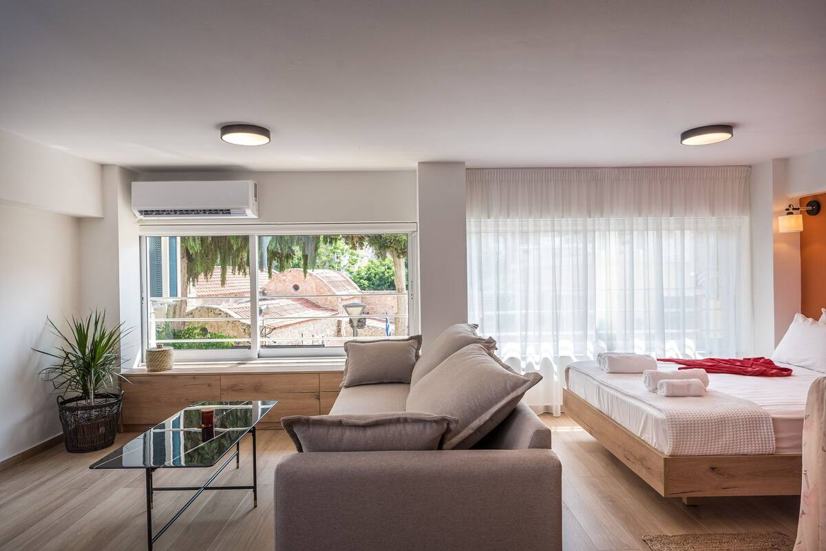 Ein modernes Zimmer mit einer Couch, einem Bett, einem Glastisch und einer Zimmerpflanze.