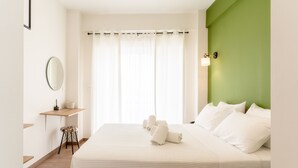A bedroom with a bed, a bedside table, a mirror, and a green accent wall. - Senaon Urban Living City Center (Heraklion)
