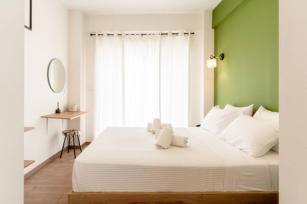 Ein Schlafzimmer mit einem Bett, einem Nachttisch, einem Spiegel und einer grünen Wand als Blickfang.