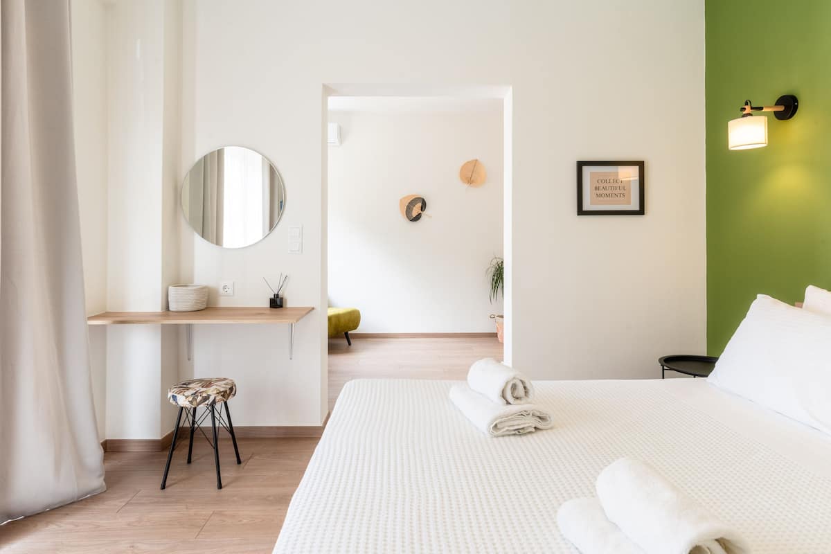 Ein modernes Hotelzimmer mit einem großen Bett, einem Schreibtisch mit Stuhl, einem runden Spiegel und einer Wand in Grünton.