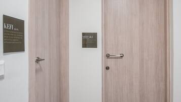 A hallway with two wooden doors, each with a metal handle and a nameplate. There are black doormats on the floor.