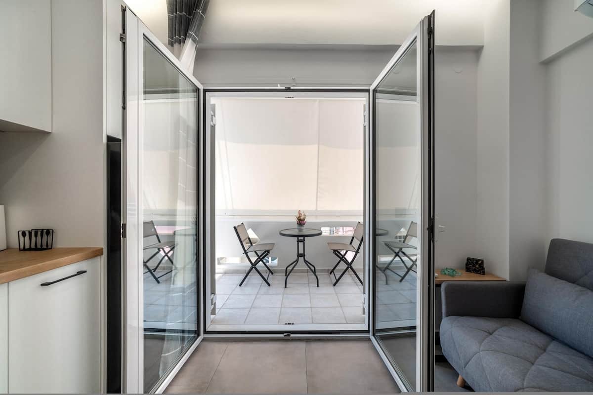 Un appartement moderne doté d’un balcon aménagé avec une table et des chaises, un canapé et un coin cuisine comprenant des placards et un plan de travail.