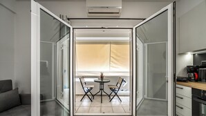 Un interior moderno con una puerta corrediza de vidrio que da a un balcón con mesa y sillas, un sofá y una kitchenette.