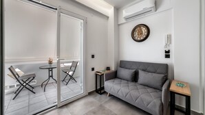 Una sala moderna con un sofá gris, una mesita de madera y un ventanal de vidrio que da a un balcón con dos sillas.