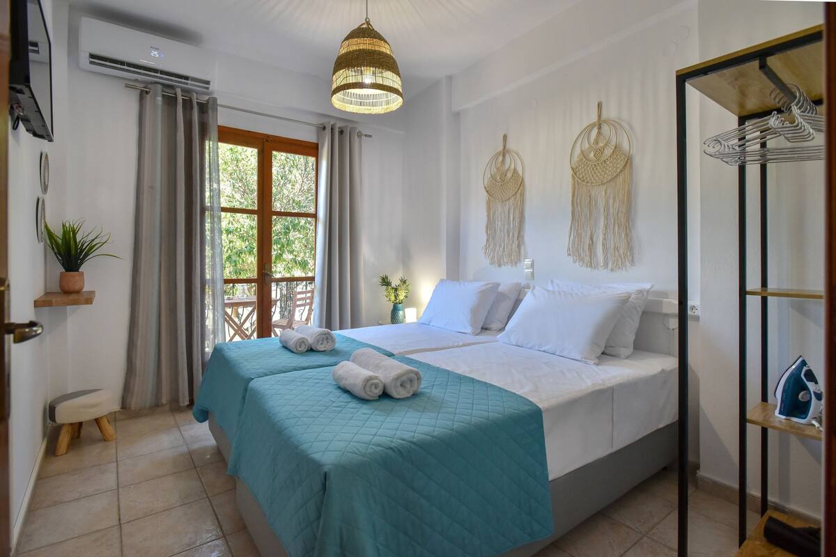 A bedroom with a bed, a hanging light fixture, a macrame wall hanging, and a window with curtains.