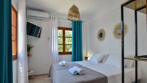 A hotel room with two beds, a TV, an air conditioner, and a window with curtains. - Eva Studios & Apartments by Cretan Houses (Malevizi)