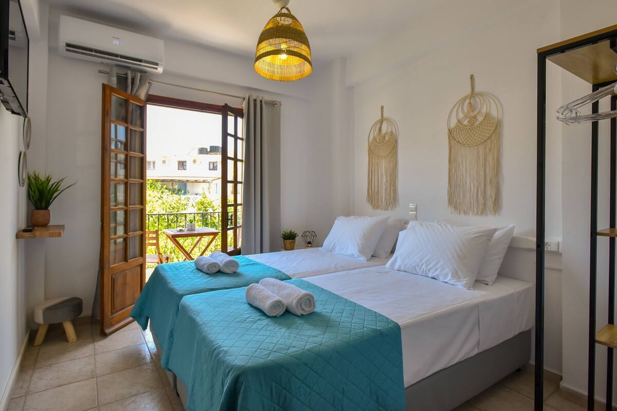 A bedroom with two beds, a balcony, a hanging light fixture, and a wall-mounted air conditioner.
