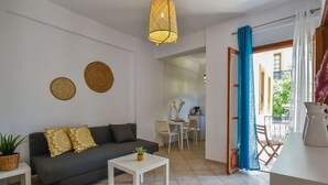 A modern living room with a sofa, a coffee table, and a dining area with chairs and a table. - Eva Studios & Apartments by Cretan Houses (Malevizi)